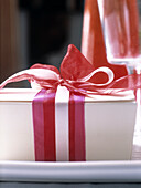 Weiße Geschenkbox mit rosa und roten Bändern auf einem Esstisch