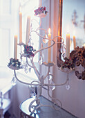 Decorative metal chandelier with cut glass pendants and lighted candles in front of baroque mirror