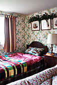 Karierte Decke und Steppdecke auf Einzelbett unter Kunstwerk mit schleppendem Laub in Shropshire cottage England UK