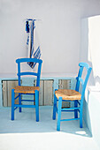 Zwei blaue Stühle im weiß getünchten Innenhof einer griechischen Villa