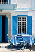 Blaue Klappstühle am Tisch vor einer sonnenbeschienenen griechischen Villa