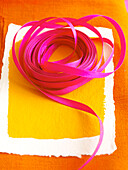 PInk ribbon on yellow painted paper with orange fabric