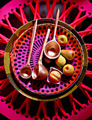 Gold metallic spoons and artificial fruit on brightly patterned plate