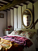 Large mirror above bed with assorted covers in timber framed farmhouse