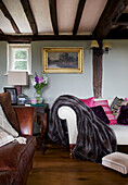 Fur blanket on white sofa below gilt framed artwork in beamed living room in Sandhurst cottage, Kent, England, UK