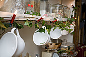 Teacups hang from shelving with fairylights in kitchen of Tenterden home, Kent, England, UK