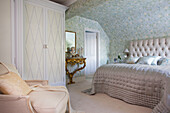 Silver quilt on double bed with floral patterned wallpaper in Kent home England UK