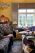 Cremefarbene und blau gemusterte Sofas mit Ponyskin im Wohnzimmer eines Bauernhauses in Etchingham, East Sussex, England, UK