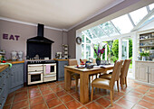 Tisch und Stühle mit schwarzer Dunstabzugshaube über dem Herd und offenen Türen in der Küchenerweiterung eines Hauses in Staplehurst, Kent England UK