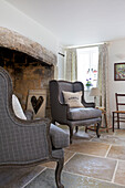 Zwei grau gepolsterte Sessel mit geschnitztem Herz am Kamin in Dorset Cottage Corfe Castle England UK