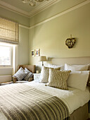 Striped blanket on bead in room with wicker chair at window in Kensington home London England UK