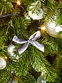 Silver bow and fairylights with baubles on Christmas tree in London home England UK