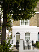 Schmiedeeisernes Metalltor und Baum an der Fassade eines weiß gestrichenen Stadthauses im Norden Londons England UK