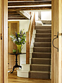 Holzgeländer und Schnittblumen mit braunem Teppichboden auf einer Treppe in einem Bauernhaus in West Sussex, England, Vereinigtes Königreich