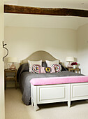 Upholstered blanket box at foot of double bed with embroidered cushions in timber- framed West Sussex farmhouse, England, UK