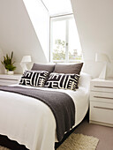 Black patterned pillows on double bed below dormer window of London home, UK