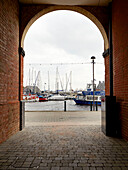 Blick durch eine gewölbte Backsteingasse auf vertäute Boote im Hafen von Ipswich, Suffolk, England, UK