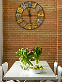 Metal clock made from salvaged materials above table with tulips in Ipswich warehouse conversion, Suffolk, England, UK