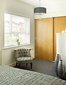 Wooden sliding doors with buttoned armchair at window in Manchester bedroom, England, UK