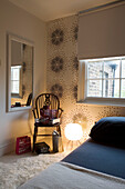 Lit lamp and chair with rectangular mirror in bedroom of London home UK