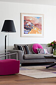 Pink armchair and cushions with grey sofa and black standard lamp in living room of Newmarket home Suffolk UK