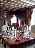 PInk flowers and place settings on polished antique dining table in East Sussex home, England, UK