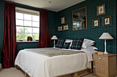 Red curtains at window of Suffolk bedroom with artwork displayed above bed UK