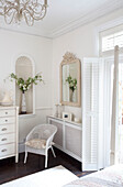 Cut flowers in niche with chair and radiator cover, bedroom of Surrey home, England, UK