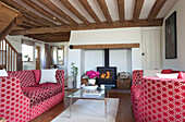 Rot gemustertes Sofa mit gläsernem Couchtisch in einem Holzbalkenhaus in Kent, Großbritannien