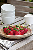 Schale mit Erdbeeren mit Keramikschalen und Milchkännchen auf einem Holztisch im Garten in London, UK