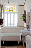 Sunlit bathroom with original stained glass windows, washstand and freestanding bath in London townhouse, England, UK