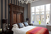 Striped wall paper and carved wooden headboard in London townhouse bedroom