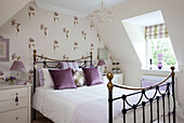 Brass bed in floral wallpapered contemporary attic bedroom of Kent cottage, England, UK