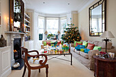 Lit candles and Christmas presents with tree in London living room with lit fire, UK