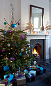 Presents under Christmas tree next to lit fire in London home, UK