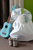 Light blue guitar and sack of Christmas presents on floor with slippers in contemporary London home, UK
