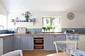 Herbs on windowsill of blue fitted kitchen in Sussex cottage, England, UK