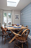 Wooden dining table and chairs with blue patterned wallpaper in London townhouse, England, UK