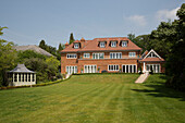 Hinterer Garten mit Rasen und Backsteinfassade eines Landhauses in Surrey, England, Vereinigtes Königreich