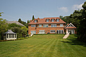 Lawned back garden and brick exterior of Surrey country house England UK