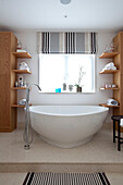pale wood shelving with contemporary freestanding bath in Surrey country home England UK