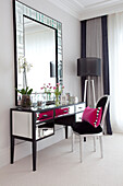 Black chair with pink cushion at mirrored dressing table with large mirror in bedroom of contemporary Surrey country home England UK