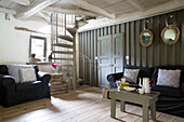 Spiral staircase in living room with black sofas in Brittany cottage, Western France