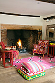 Upholstered armchairs at lit fire with floor cushions in Herefordshire home, England, UK