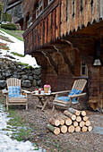 Pair of chairs with logs stacked, below carved balcony exterior of mountain chalet, Chateau-d'Oex, Vaud, Switzerland