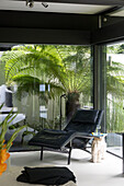 Black leather recliner with view through window to palm plant in contemporary SW London home England UK