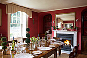 Beleuchtetes Feuer im roten Esszimmer eines Hauses in Burwash, East Sussex, England, UK