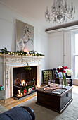 Wooden coffee table in front of fire with lit Christmas candles in London home, England, UK