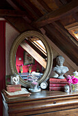Ovaler Spiegel mit Büste und gebundenen Büchern auf Schlafzimmerkommode in einem französischen Bauernhaus-Schlafzimmer