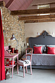 Pink desk and chair with grey double bed under ceiling beams in exposed stone bedroom of Brittany cottage, France